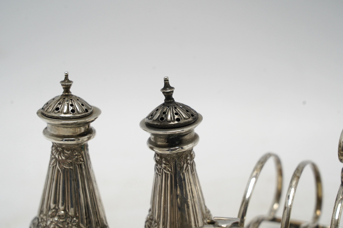 Sundry silver including a pair of Edwardian pepperettes, a five bar toast rack, a mustard pot (a.f.), a pair of sugar tongs and a cover. Condition - poor to fair